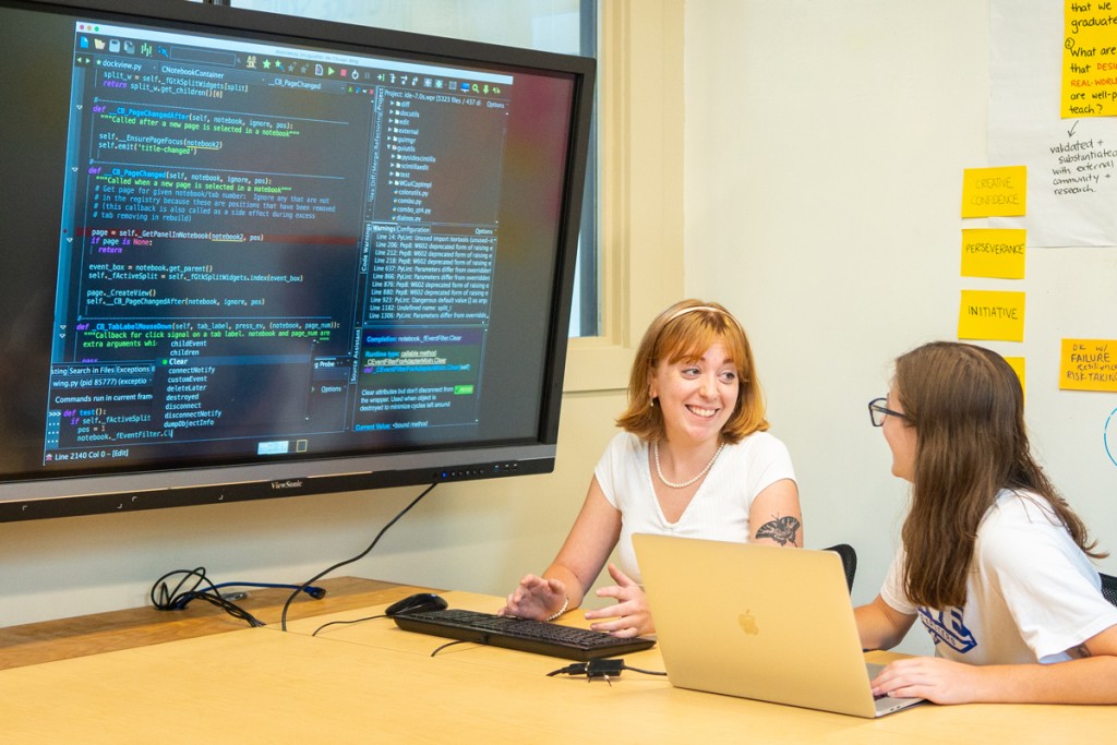 Two students review computer programming code on a large monitor