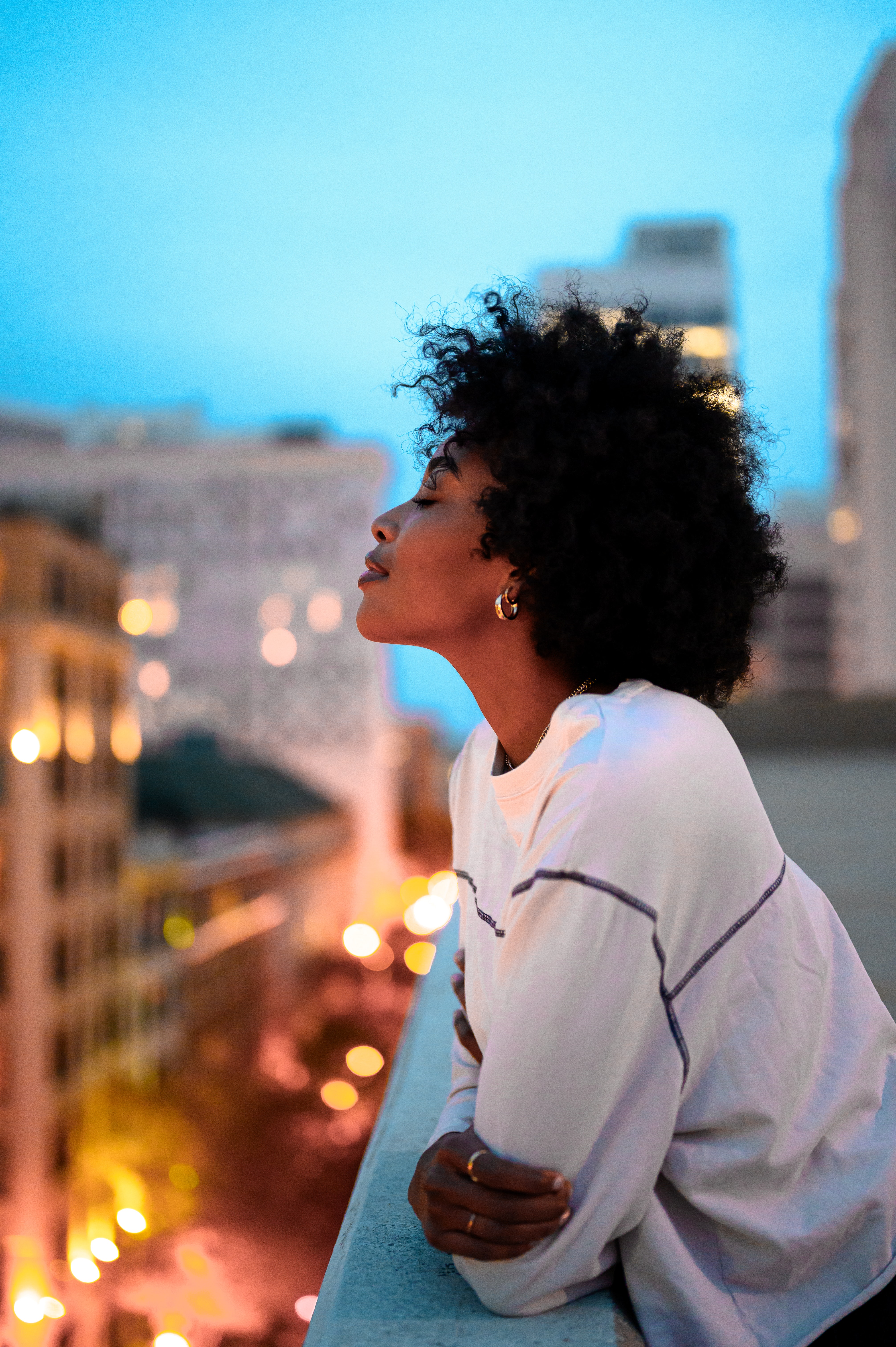An African American woman stands on a city balcony at dusk