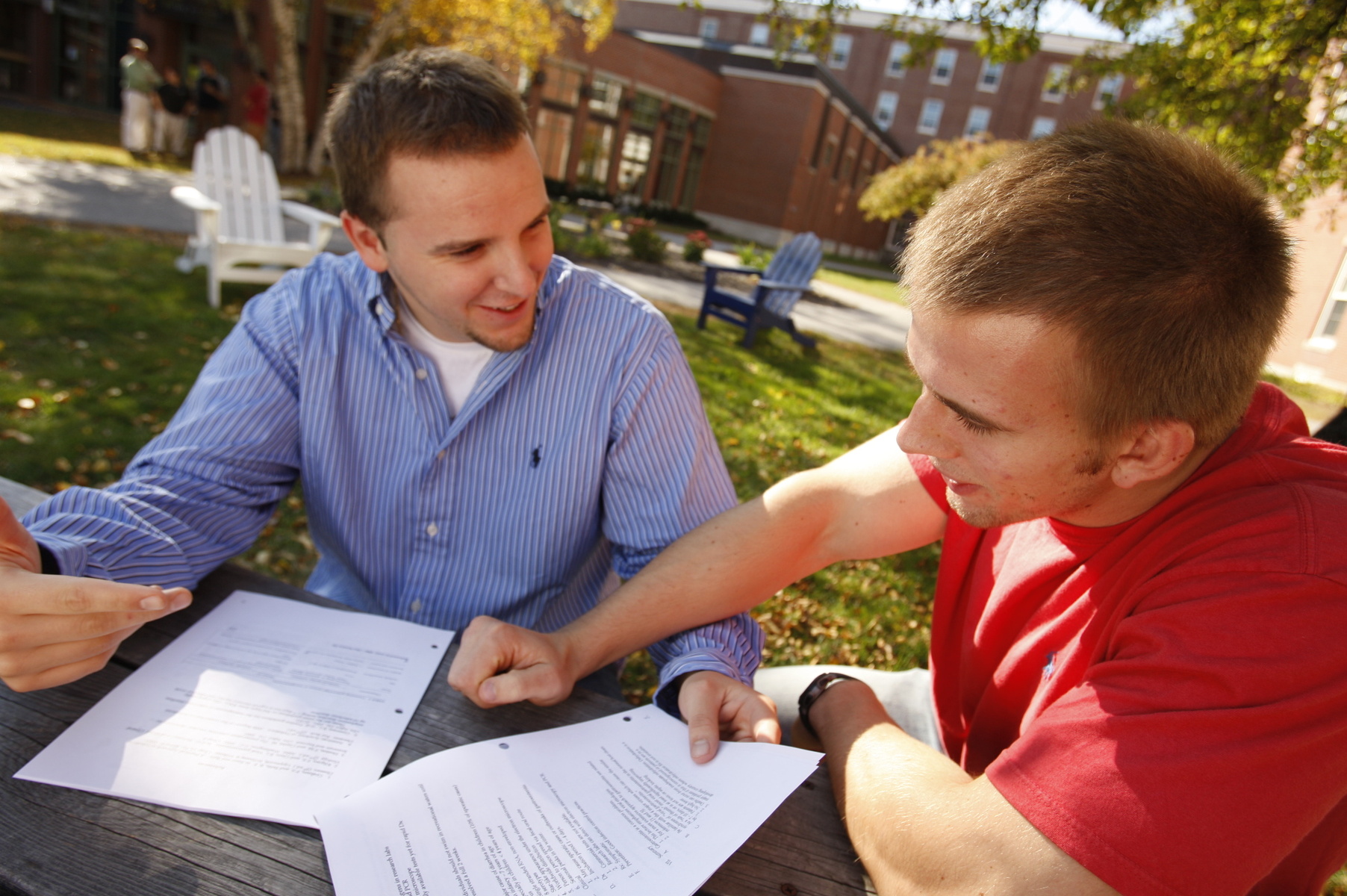 Two male students sit outside on a nice day looking at some classwork
