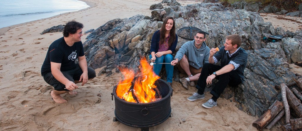 a group of students sit around a bonfire on the beach