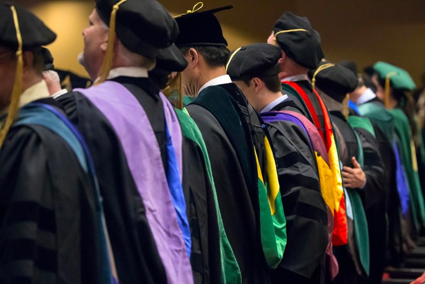 The backs of a group of C O M students at their hooding ceremony