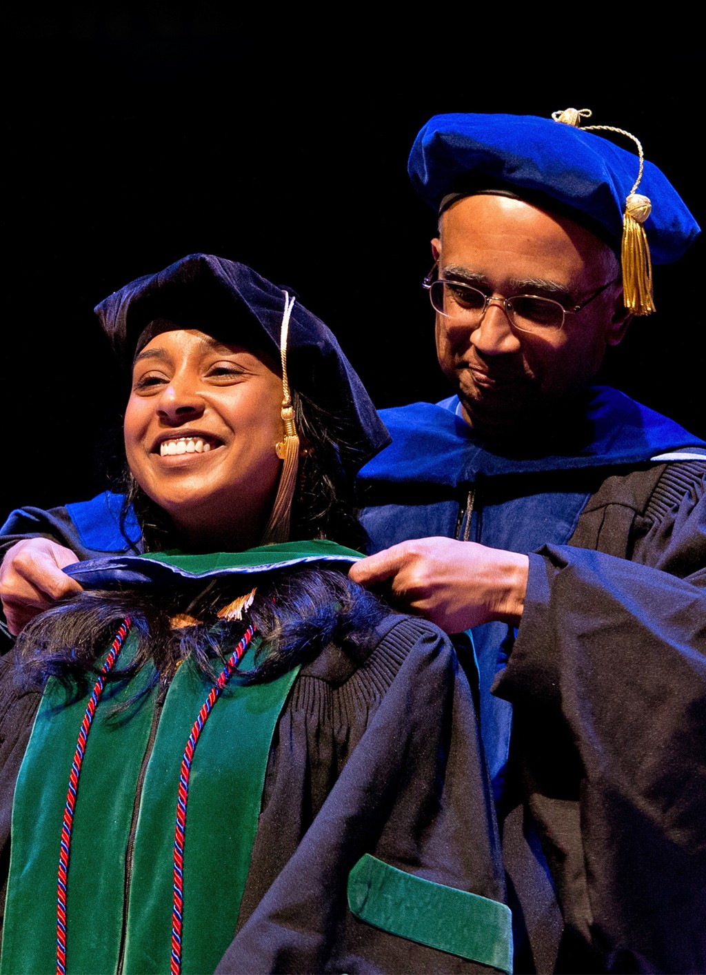 A mentor places a hood on a graduating C O M student