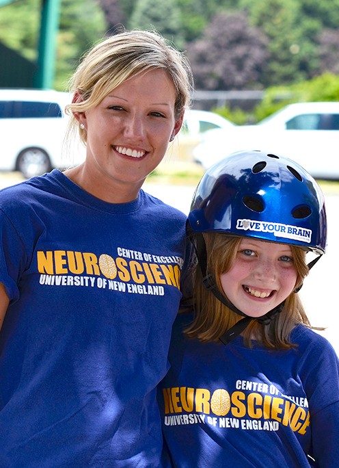 A U N E student stands with a kid wearing a bike helmet for a neuroscience outreach program