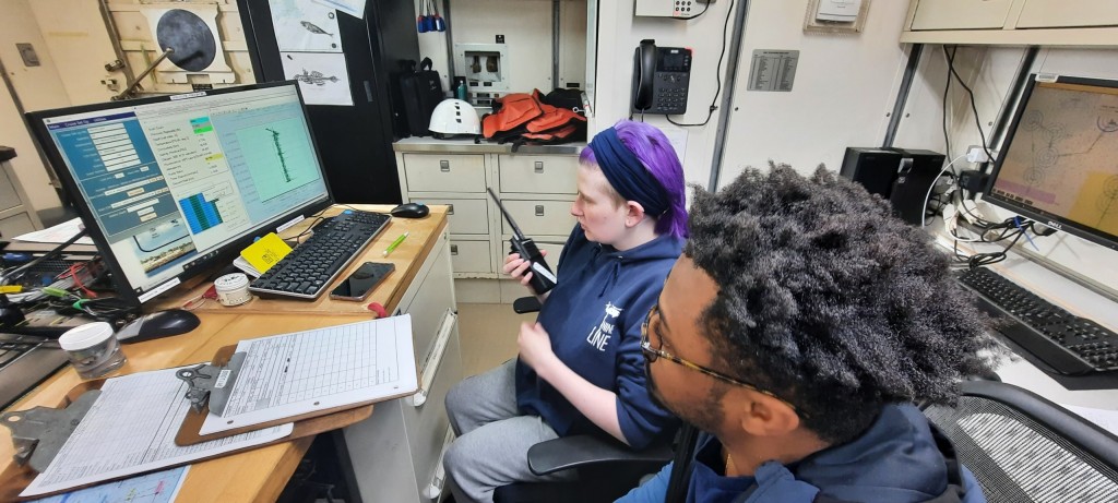 Kenzi Kimball sitting in front of computer using walkie talkie to communicate on NOAA research vessel