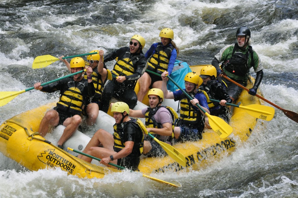 A group of U N E students having fun while white water rafting down a river in Maine