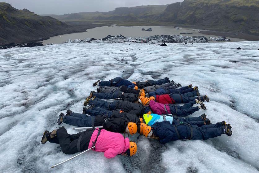 A group of students in winter gear and safety hats laying down on a lake of ice outdoors