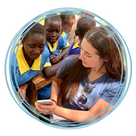 A U N E student studying abroad shows their mobile phone to a group of young children in Kenya