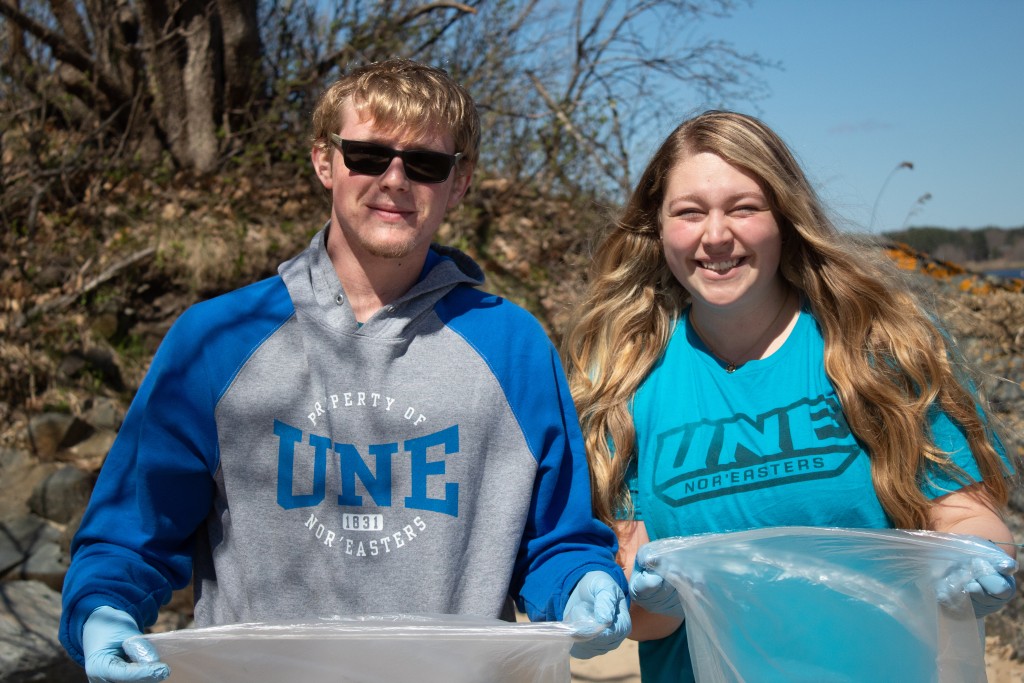 Two students smile as they hold up trash bags for a Save the Waves cleanup event