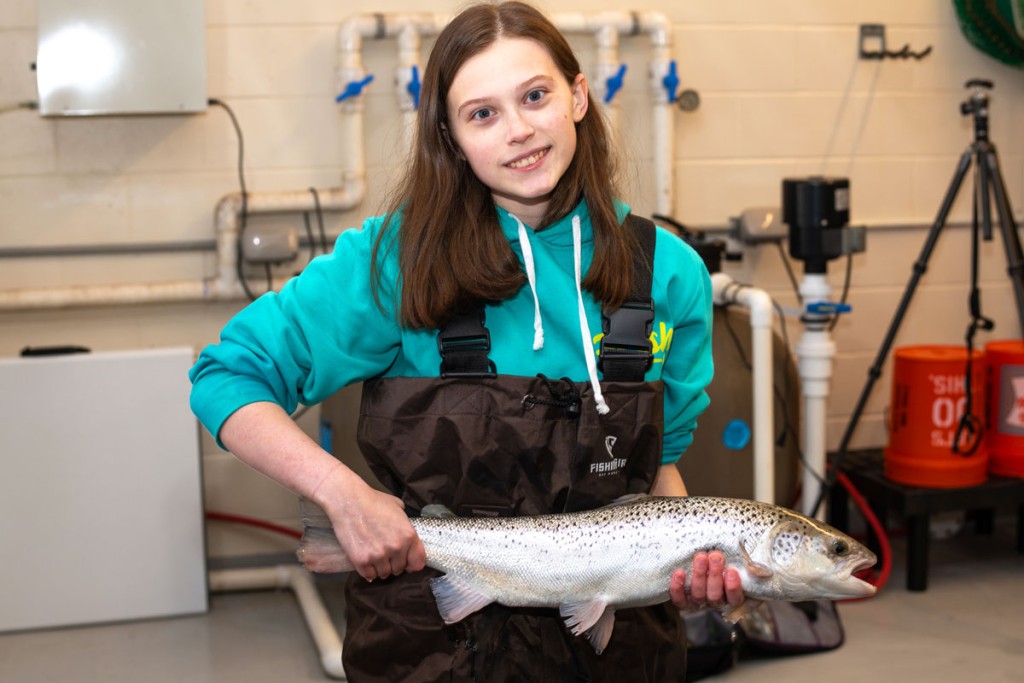 A student wearing work overalls holds up a fish in the Marine Science Center