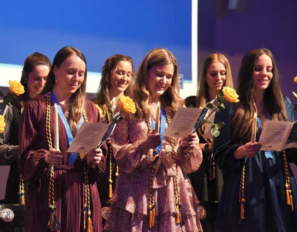 A group of students reads from their programs onstage