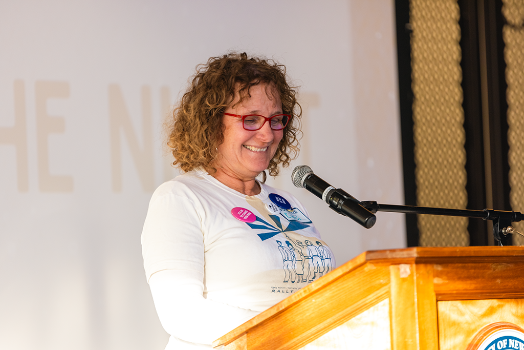 Photo of a woman speaking into a microphone at a podium