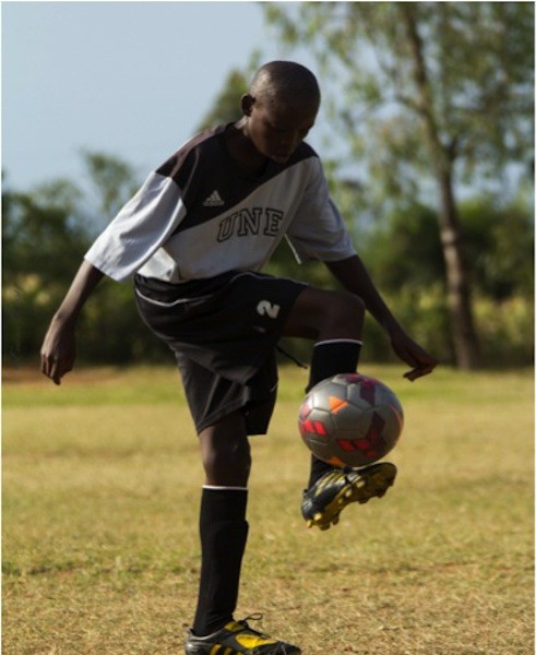 A Kenyan boy who was the recipient of a UNE soccer uniform in 2014 participates in the Football for the Environment program.