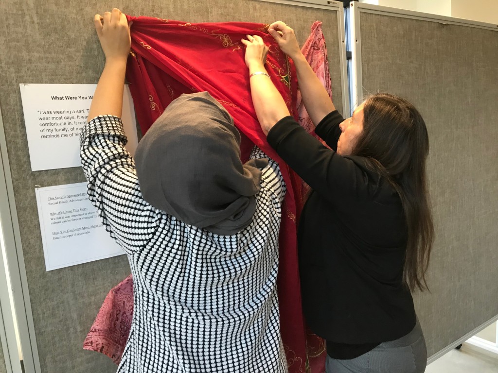 UNE's Title IX coordinator Angela Shambarger and Hajra Chand hang clothing for a display