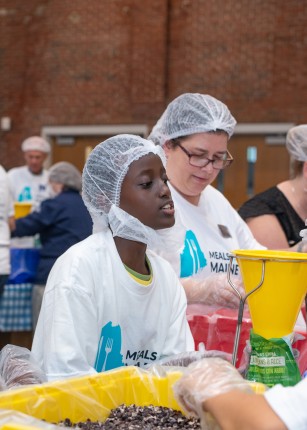 A young volunteer joins the crowd in packing meal kits
