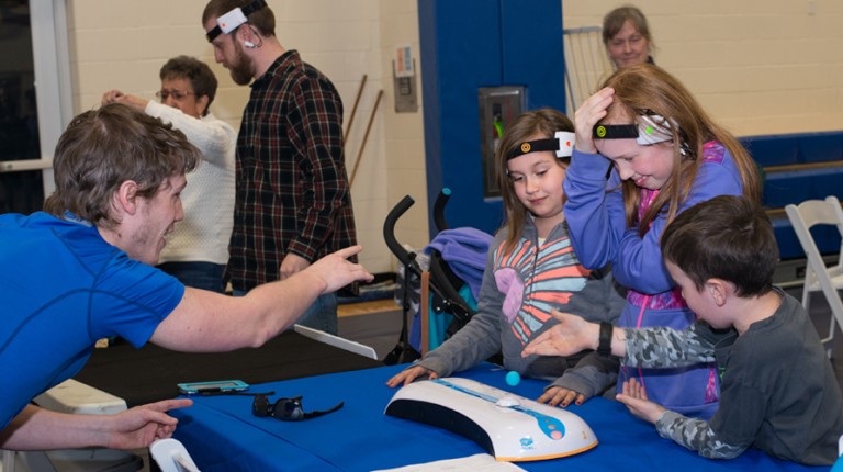 A student explains technology to three children at a U N E Brain Fair