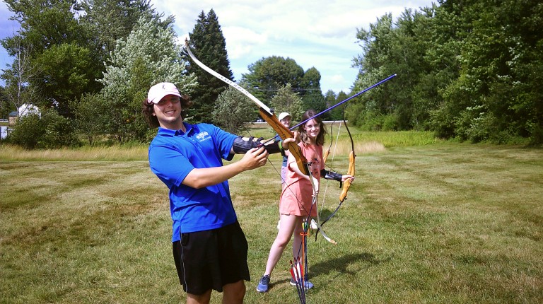 Students pose with bows and arrows in a field