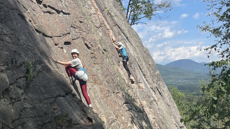 Two students scale the side of a mountain using ropes