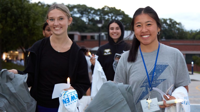 Three new undergrad students holding candles and Nor'easter t-shirts during First Night