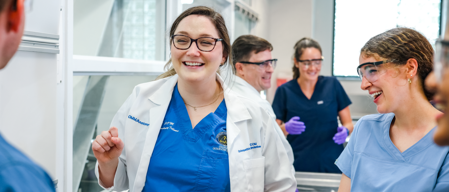 A medical student smiles with her classmates in a UNE lab