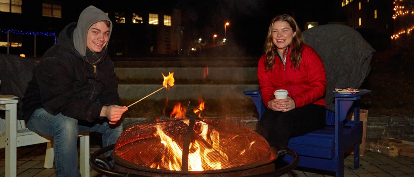 Students roast marshmallows and drink hot cocoa by a bonfire