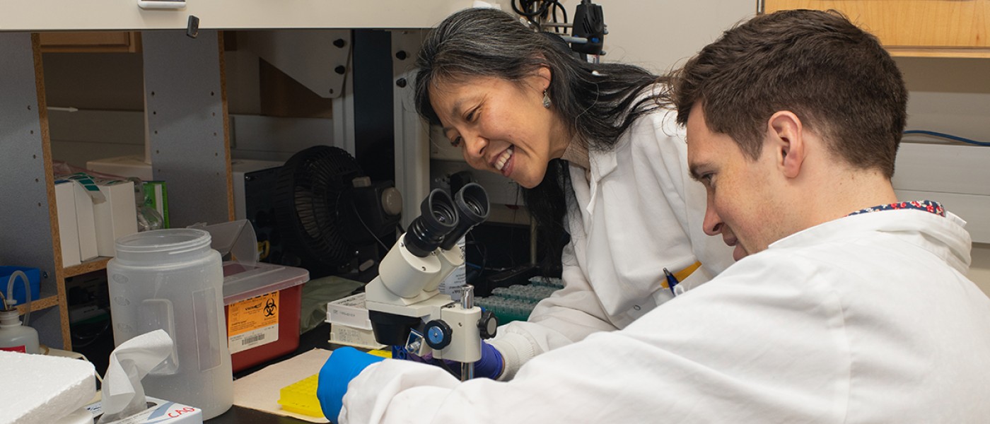 A professor helps a student prep a microscope slide
