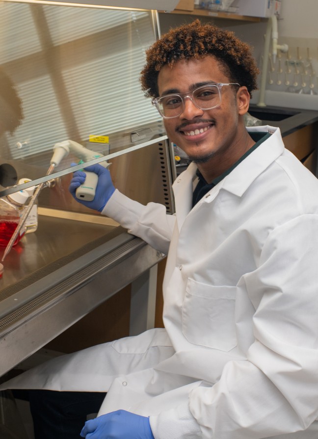 A student researcher smiles while holding lab equipment