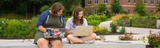 Two students on their laptops sitting outside on the Biddeford Campus