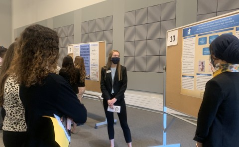 Female student presents research poster to small crowd