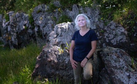 Pam Morgan leaning against a boulder in the woods