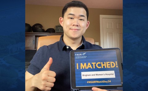 A man poses for a selfie holding a tablet displaying the words "I Matched!" while giving a thumbs up