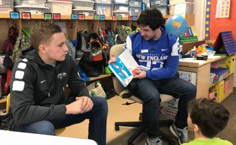 UNE student-teacher Drew Patno looks on as football player Jack Mahoney reads to children at the Eight Corners School