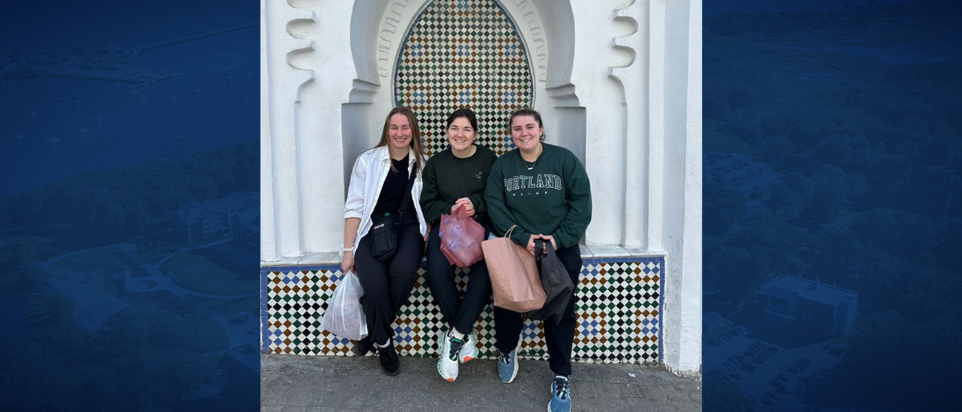 Three female students pose in front of Moroccan architecture. Photo is set against a blue background.