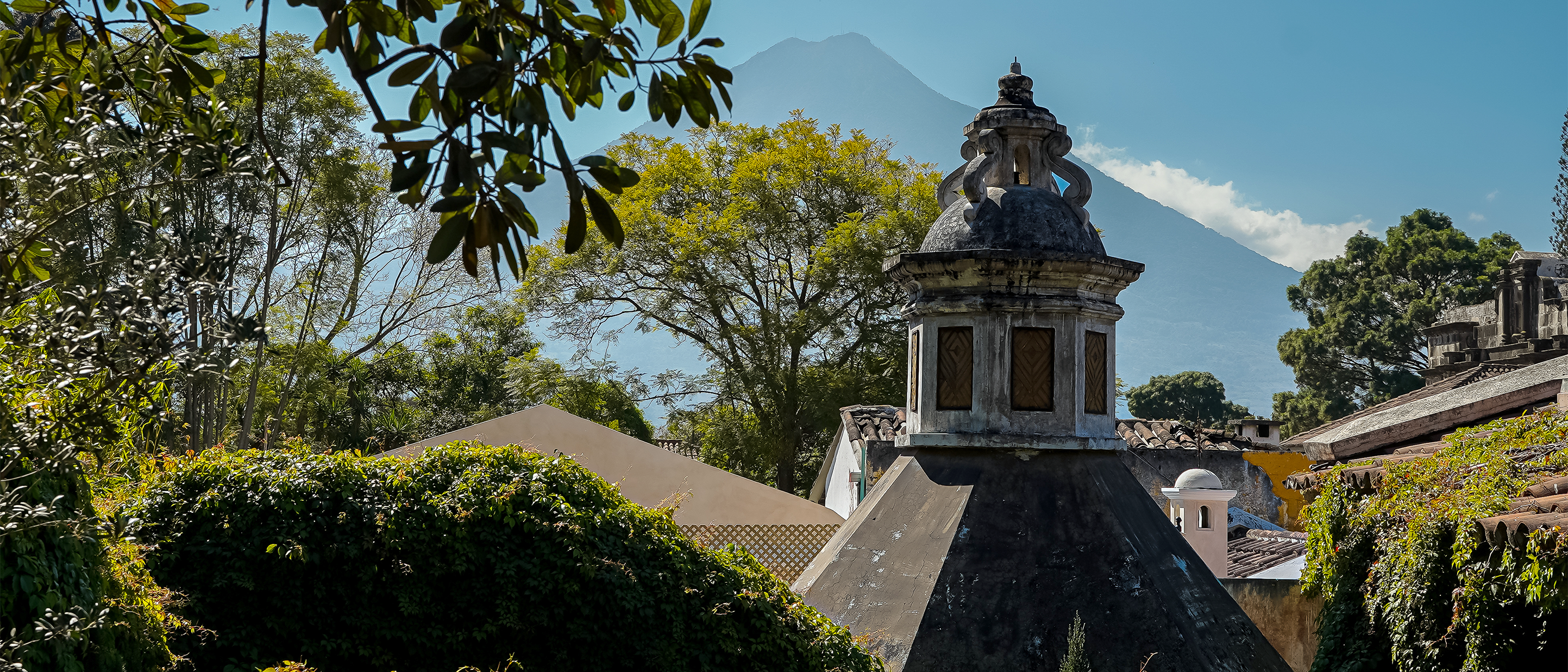 A domed colonial rooftop in Antigua, Guatemala, with a volcano rising in the distance.
