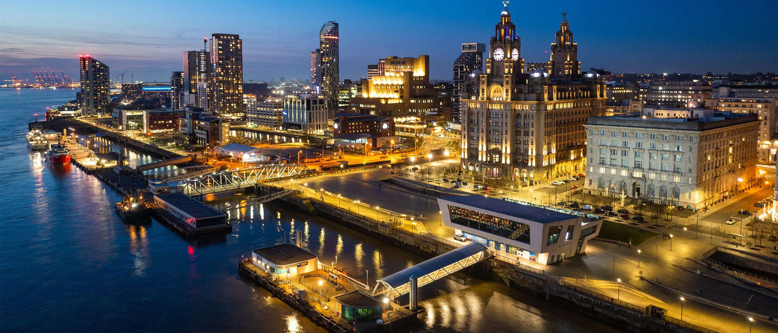 The Liverpool waterfront at night, with the illuminated Royal Liver Building and Pier Head skyline.