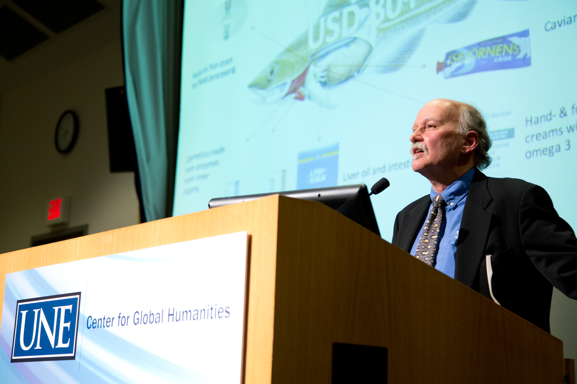 Barry Costa Peirce stands at the U N E podium to give his presentation on how climate change is reshaping maine's ocean economy