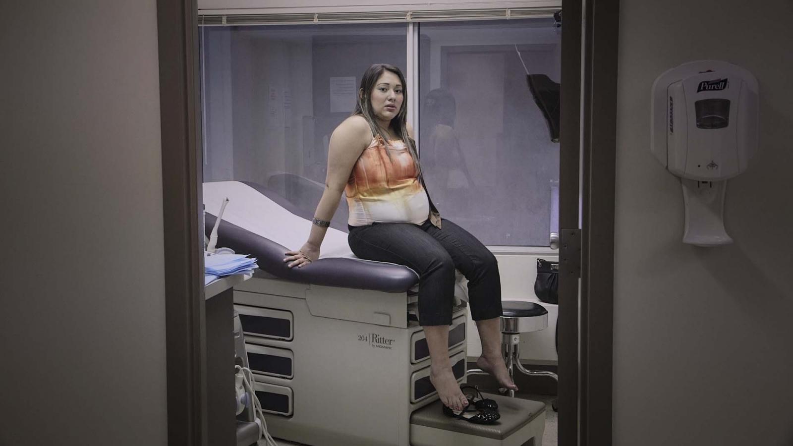 Pregnant Latina woman sits on an examination table and looks into the camera
