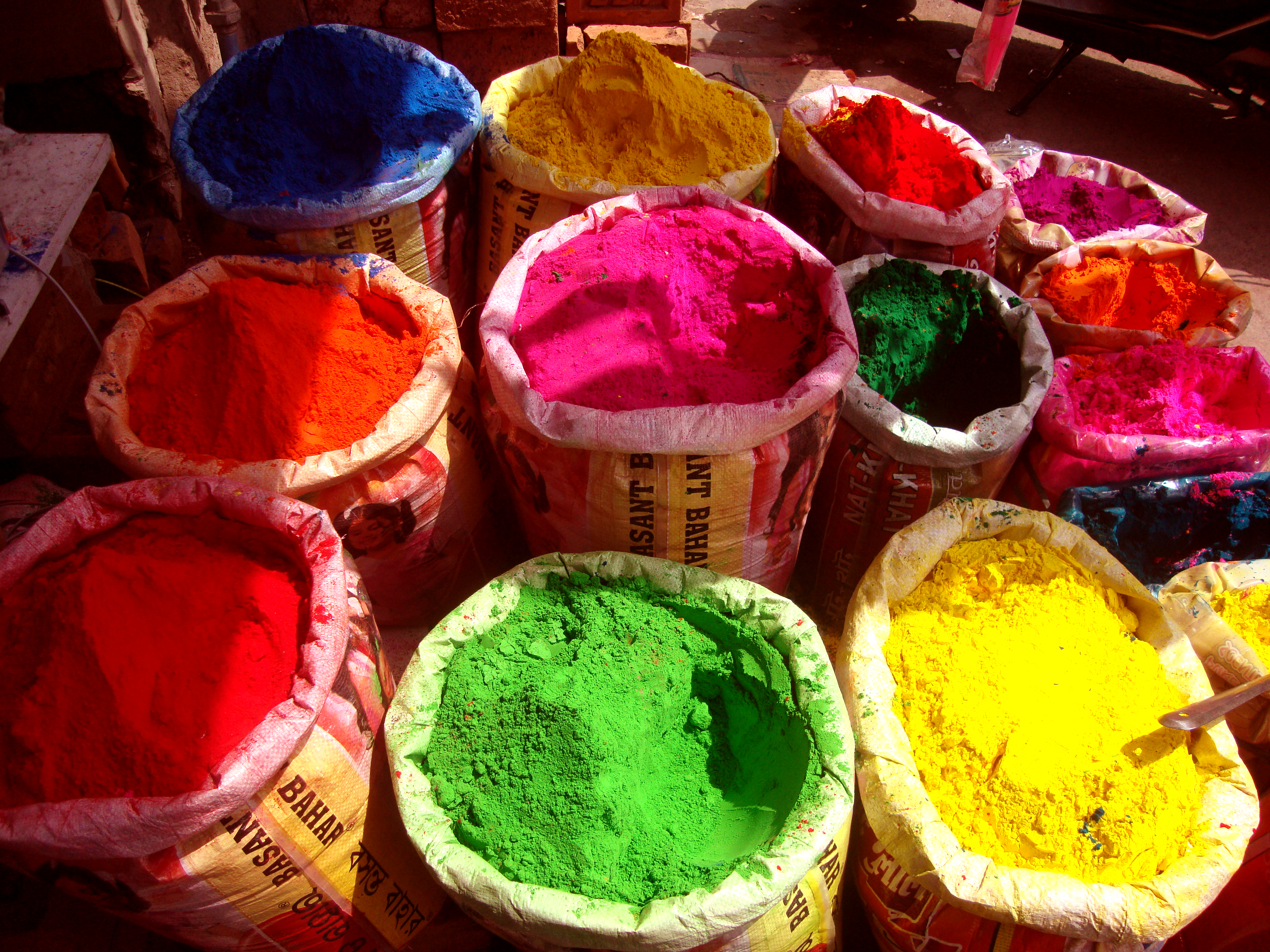 Large sacks of brightly colored powder sit in an outdoor market stall