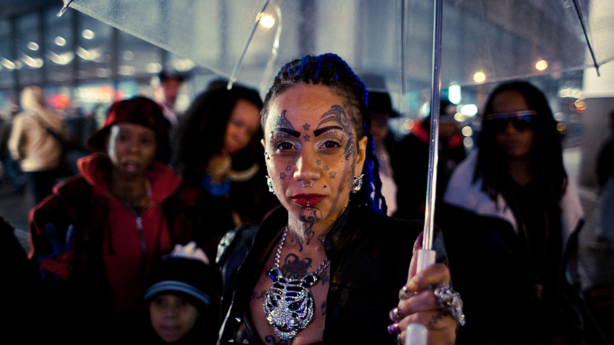 Photo of Lucky Torres, a young Puerto Rican woman with many face tattoos and long black braids. She is holding a clear umbrella.