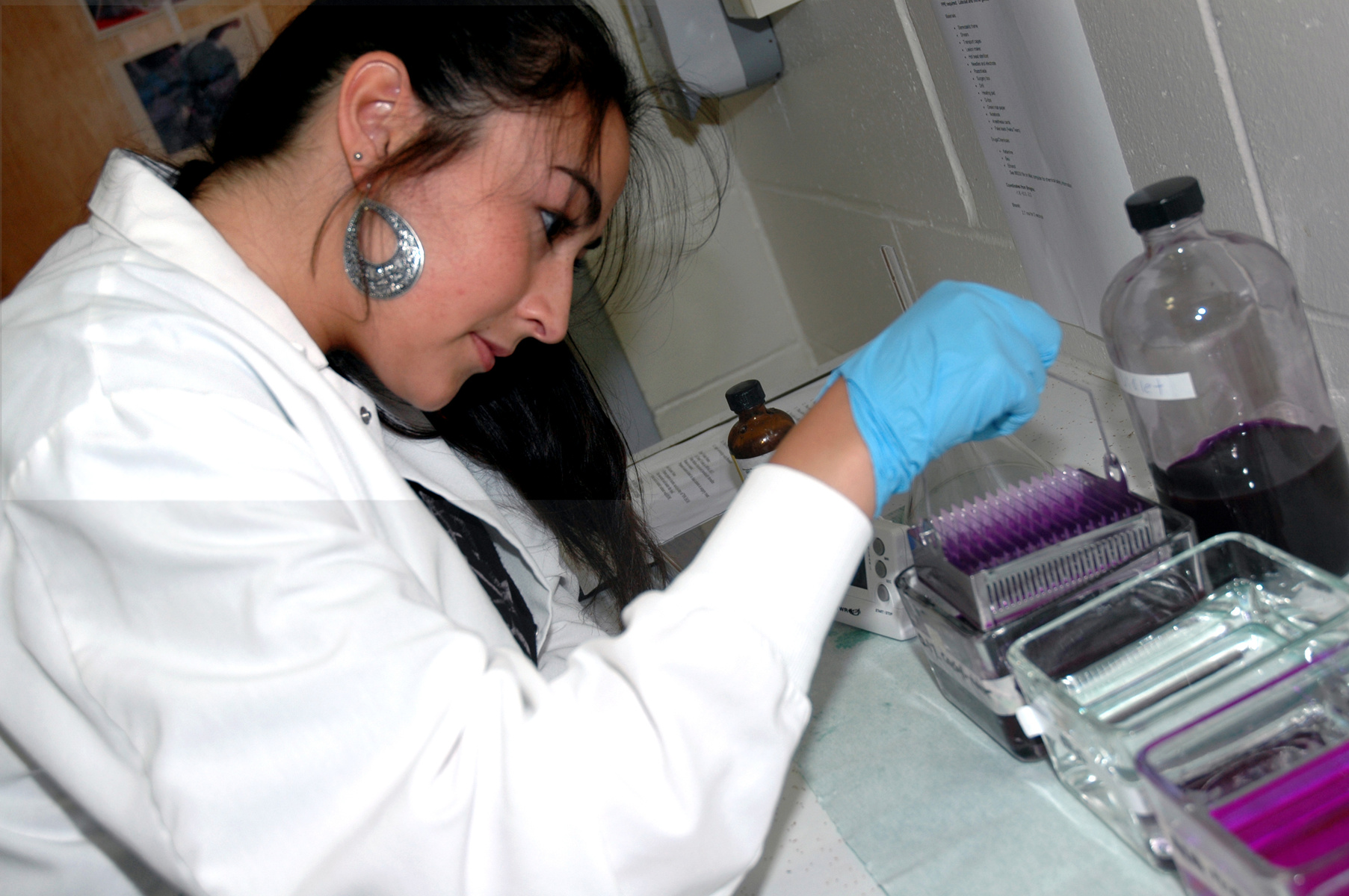 A female student in a white lab coat arranges micrscope slides in a glass case