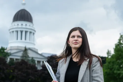 A student holds books as they stand in front of the Maine State House