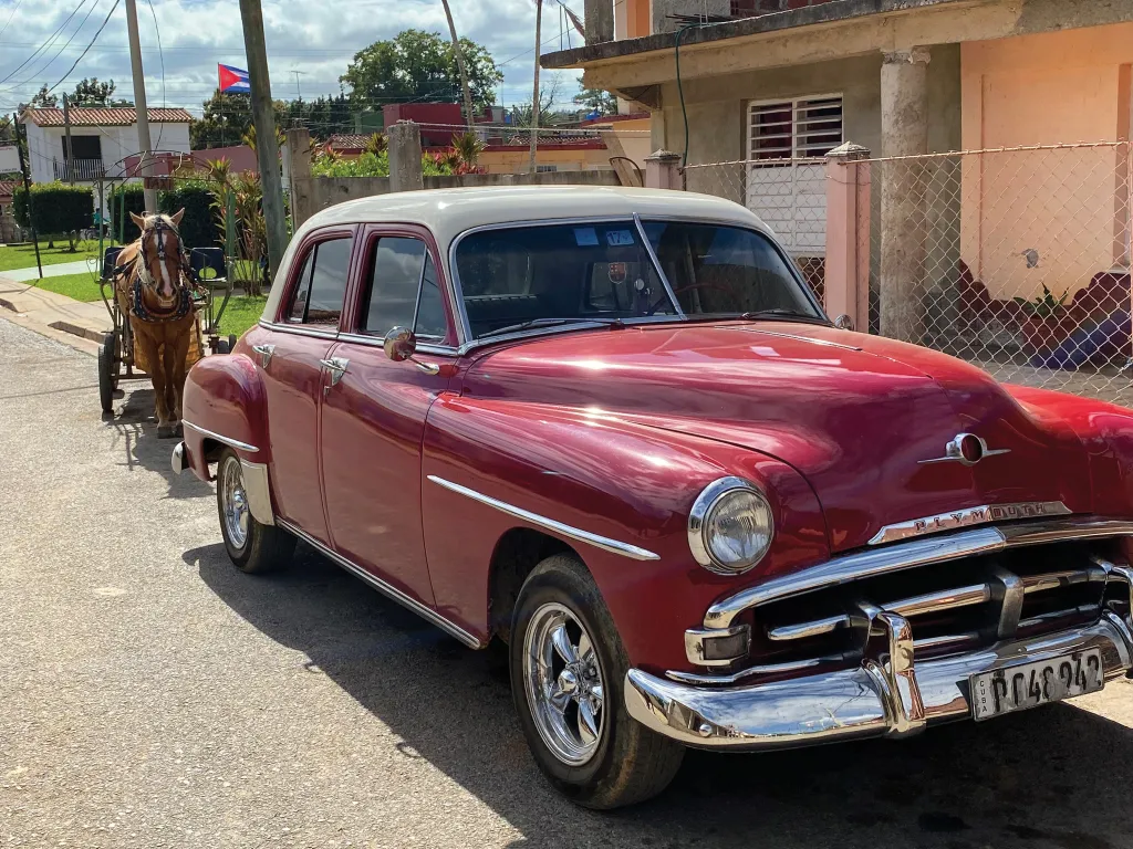 a classic red car sits in front of a horse drawn carriage on the street in Viñales, cuba
