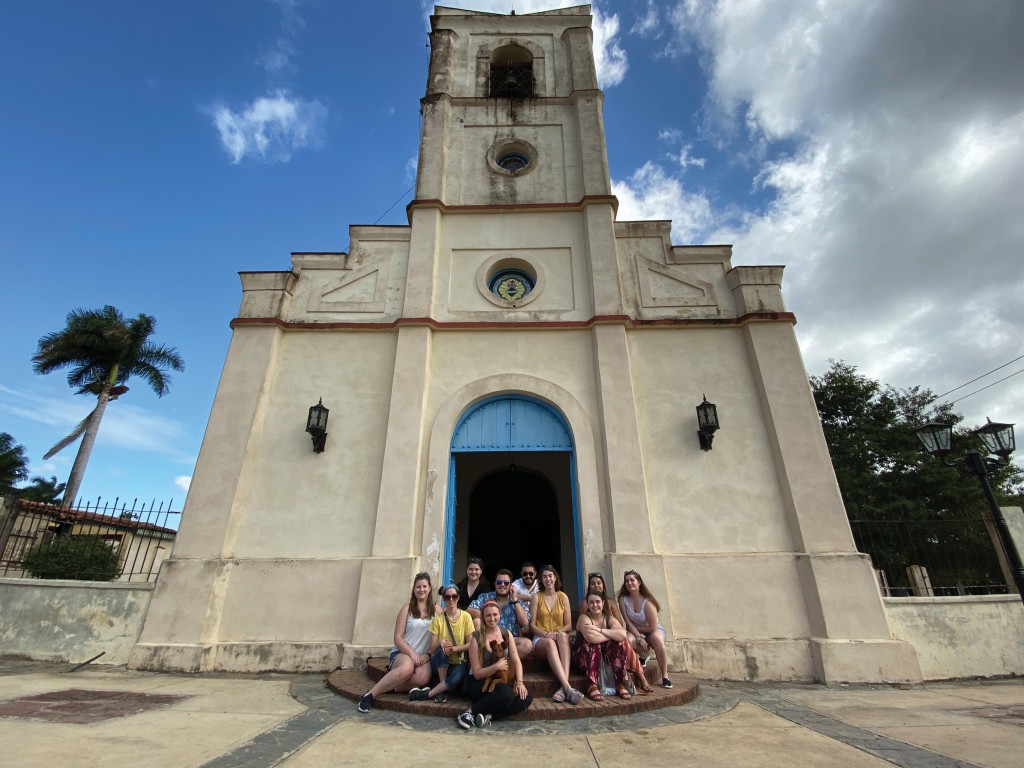 a group of students sit on the steps of a church in the center of town in  Viñales, Cuba