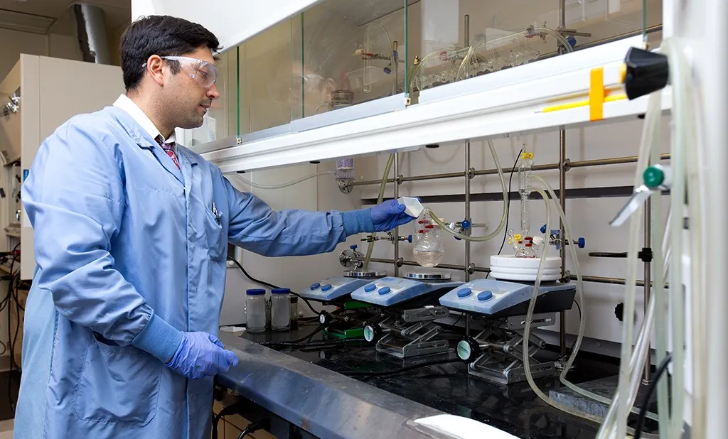 a pharmacy student wearing scrubs and safety goggles works in the lab