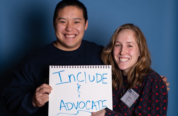 two u n e social work students pose with a handwritten sign reading include and advocate