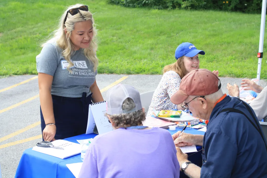 Woman stands at table talking to two adults who are sitting down