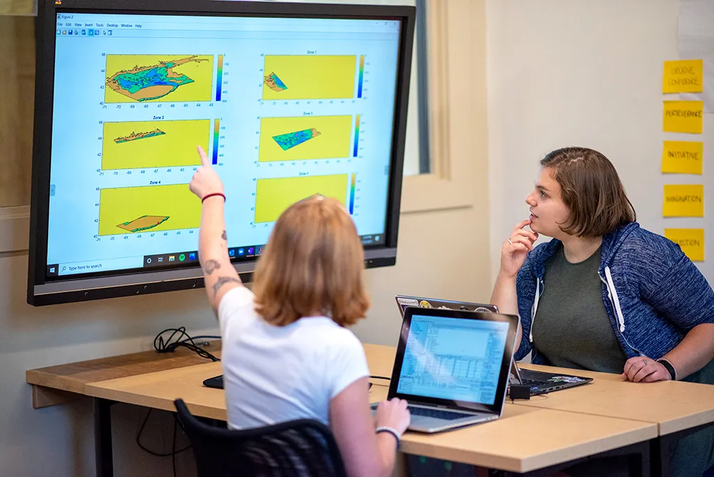 Two students study charts on a large screen