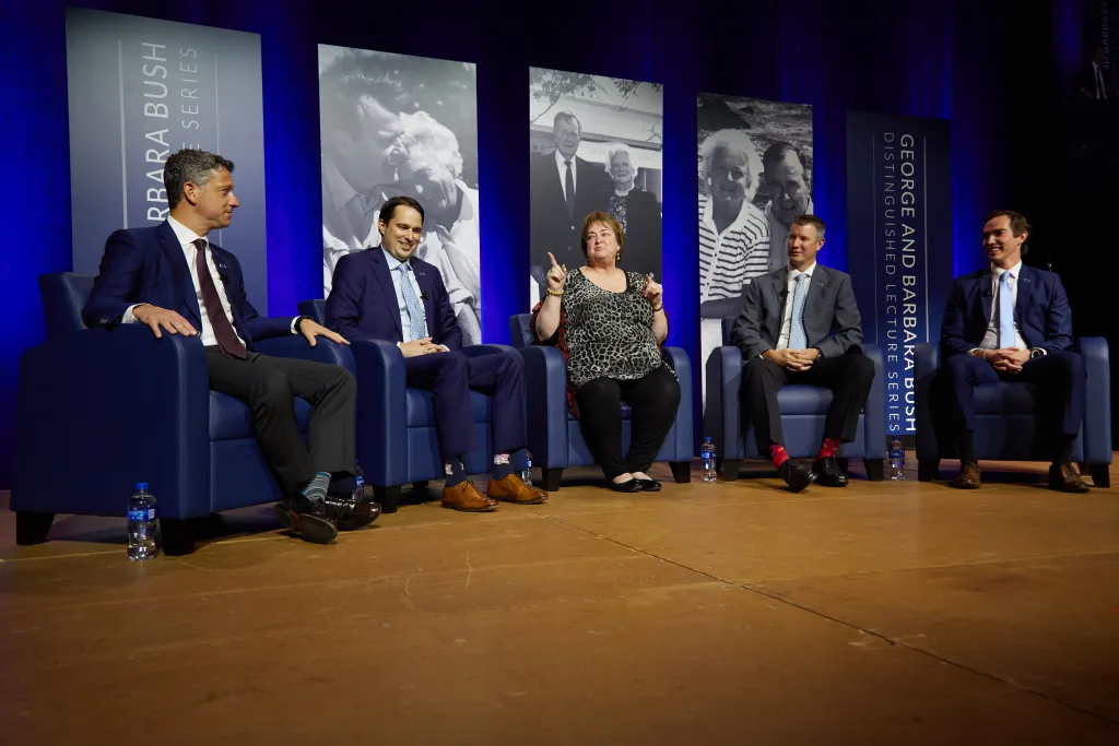 Four people sit in chairs onstage talking