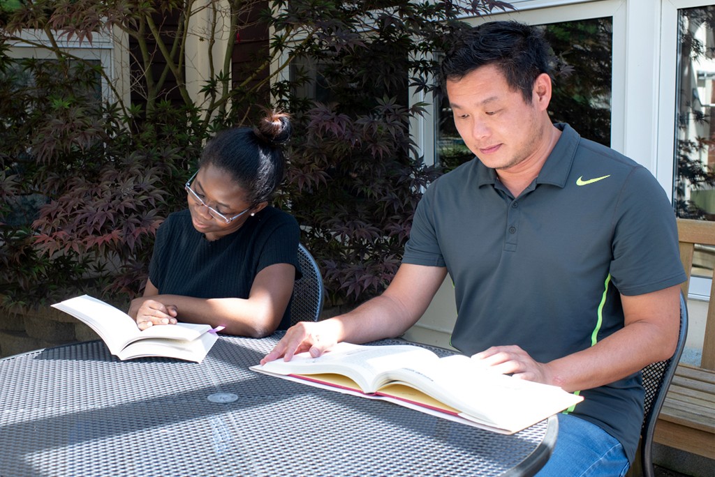 Two U N E students sit together at an outside table each reading a textbook