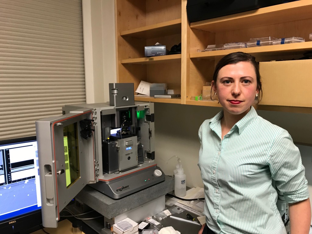 Eva Rose Balog stands next to a state-of-the-art Atomic Force Microscope