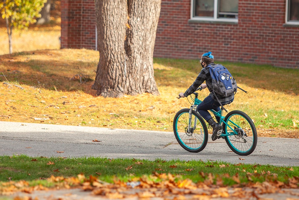 U N E student riding a bicycle through Biddeford Campus